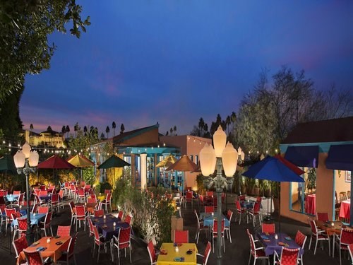 An outdoor restaurant patio with colorful tables and chairs, decorated with lights and umbrellas at sunset.