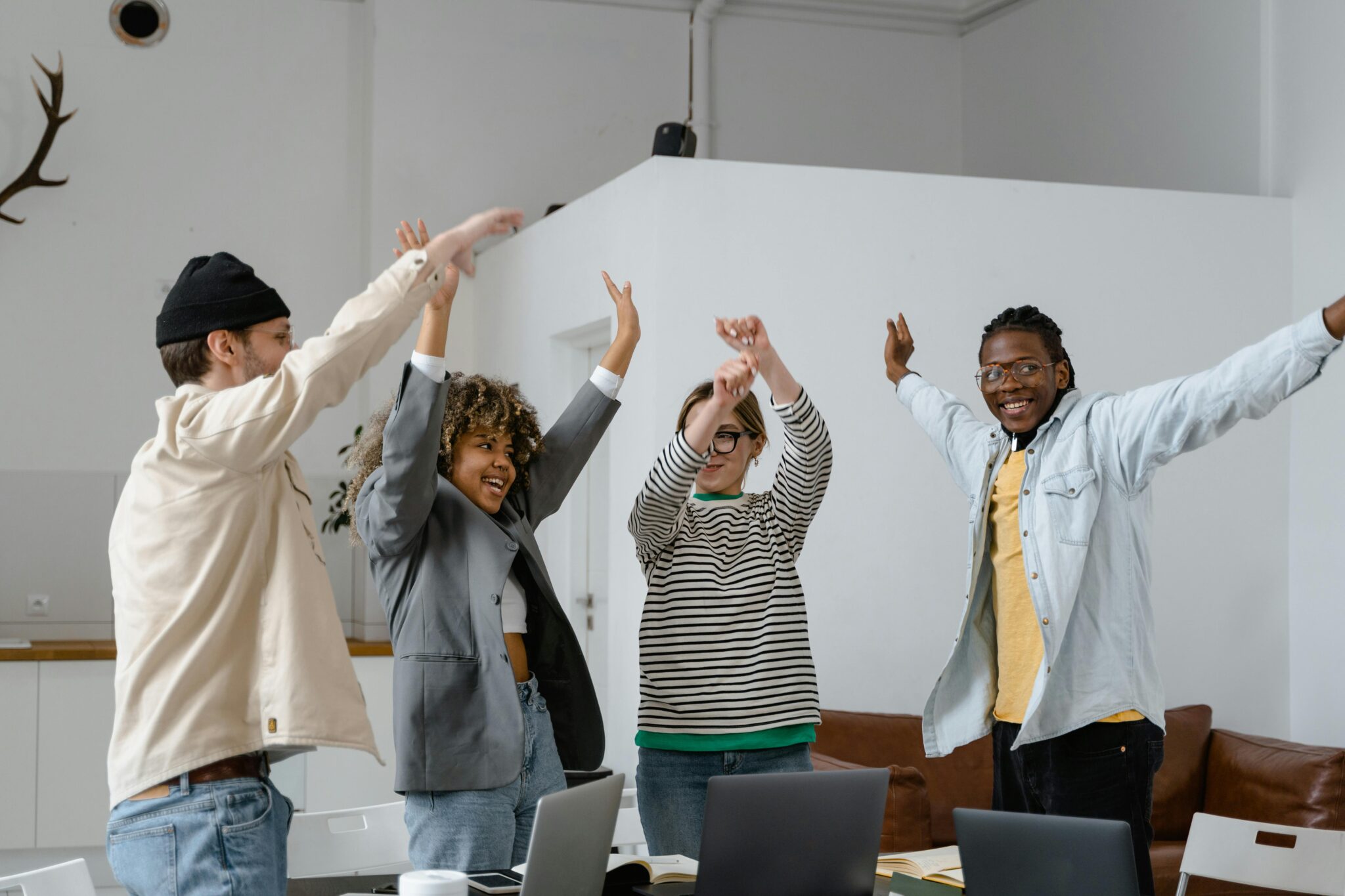 Four happy coworkers standing in an office, raising their arms and celebrating together.